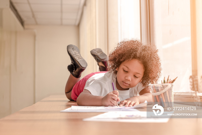 Little toddler girl laying down concentrate on drawing.  Mix African girl learn and play in the pre-school class. Children enjoy hand writing. 3 years girl enjoy playing at nursery.