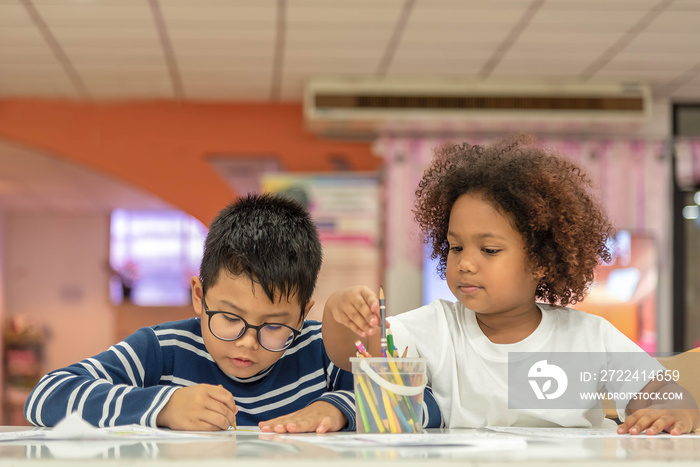 Little toddler girl and boy drawing together.  Asian boy and Mix African girl learn and play together in the pre-school class. Children enjoy hand writing. Friendship in class.