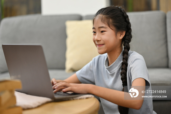 Happy Asian preteen girl school distance learning online at virtual class with teacher tutor on laptop by video conference call, watching online lesson at home.