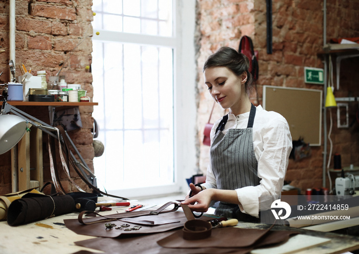 young brunette woman works in a bag making studio, cuts out details