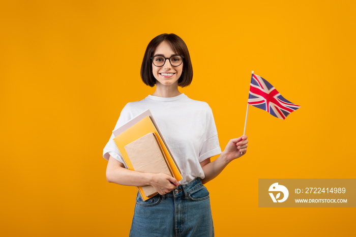 Travel and study, learn English language. Zoomer smiling woman with notebooks and small flag, orange background