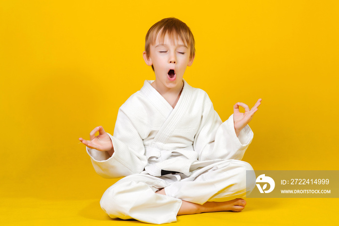 Boy in a white kimono sitting on a yellow background. Little boy practicing yoga.