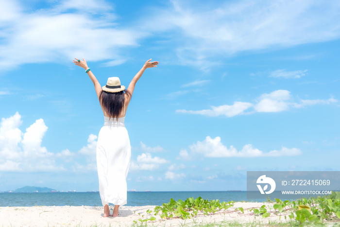 Smiling woman wearing fashion white dress summer walking on the sandy ocean beach, beautiful blue sky background.  Happy woman enjoy and relax vacation. Lifestyle and Travel Concept