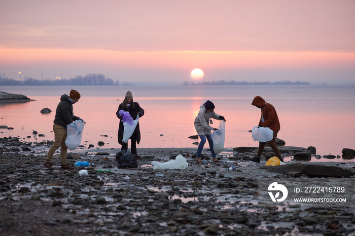 Group of volunteers picking up trash at sea shore with sunset in background, ecology and environment concept, copy space