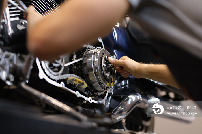 Mechanic repairs motor and chain of motorcycle in workshop