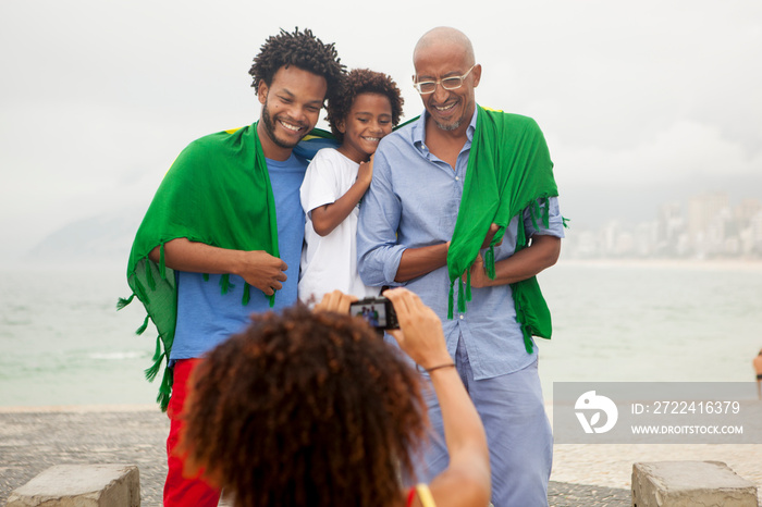 Over shoulder view of mother photographing family wrapped in Brazilian flag on Ipanema beach, Rio De Janeiro, Brazil