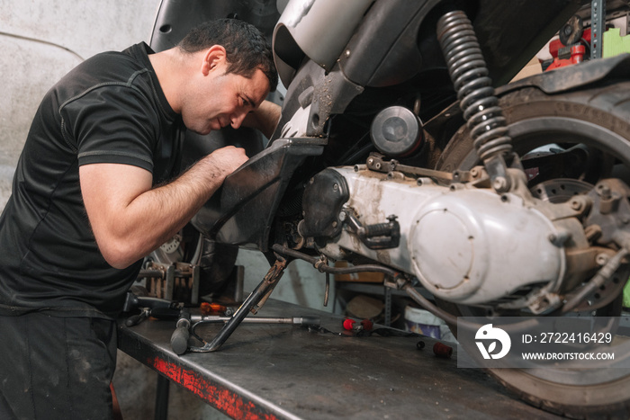 Mechanic repairing scooter motorbike in repair garage .