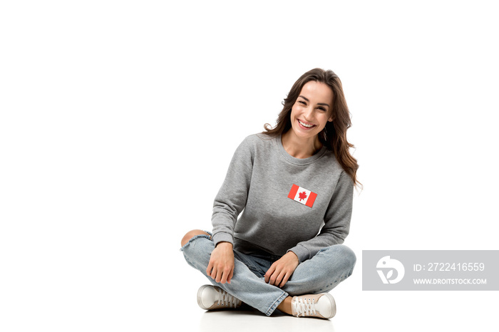 happy woman with canadian flag badge sitting and looking at camera isolated on white