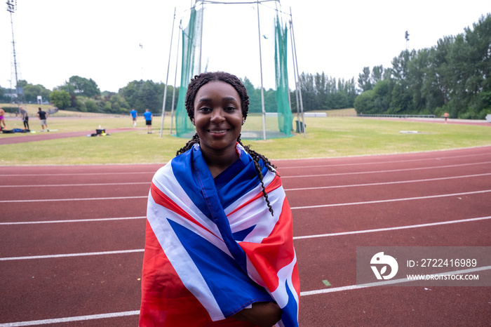 Portrait of smiling athletic�woman wrapped in British flag on running track