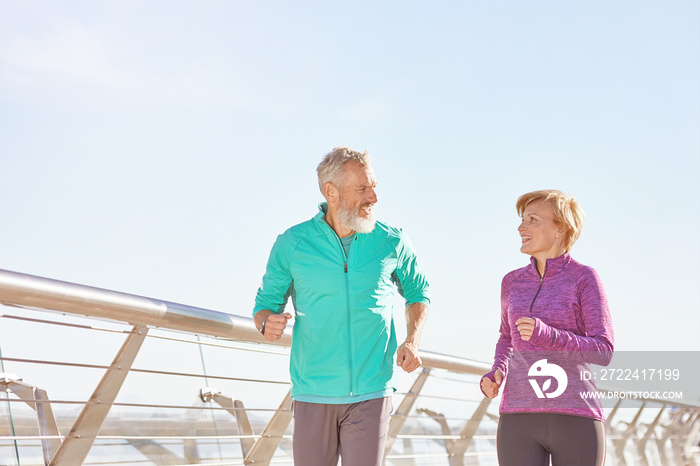 Energize your life. Active mature family couple in sportswear smiling at each other while running together on a sunny morning. Joyful senior couple working out outdoors