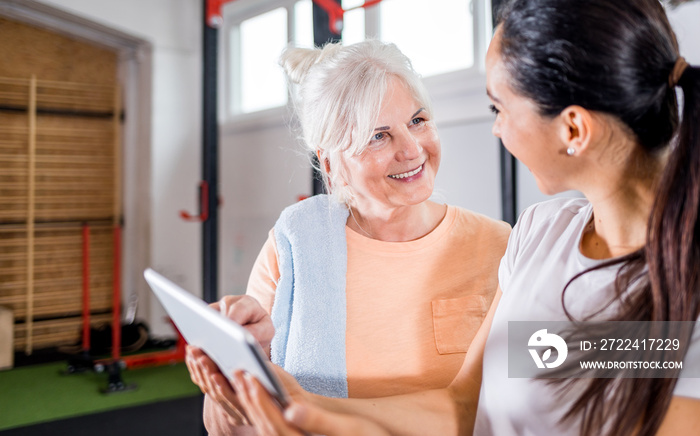 Trainer working with senior woman at the gym using tablet