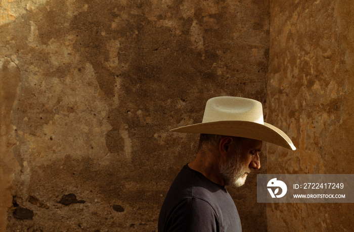 Side view of adult man in cowboy hat against wall