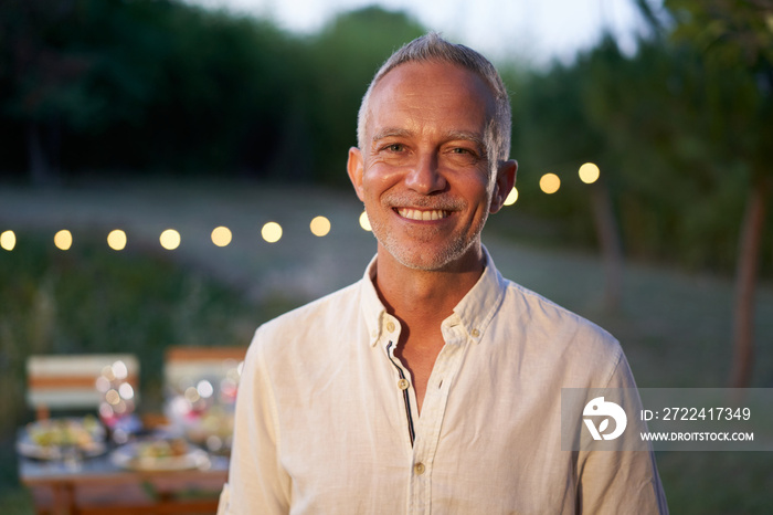 Portrait of happy mature man looking at camera outdoor. Senior people with white hair feeling confident at sunset. Closeup face of smiling with backyard in background.