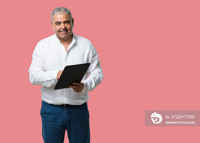 Middle aged man smiling and confident, holding a tablet, using it to surf the internet and see social networks, communication concept