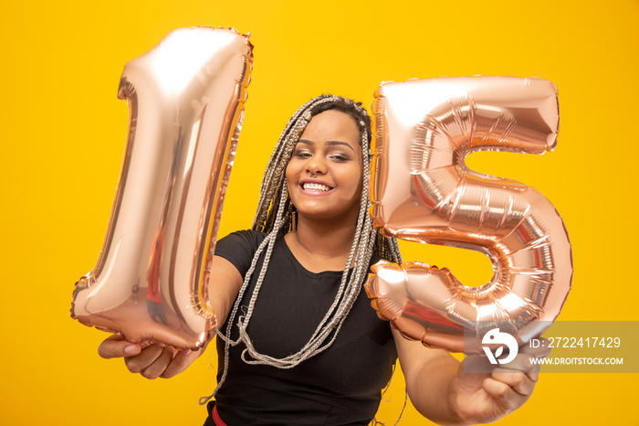 Birthday girl holding a 15 years old balloon. Yellow background.