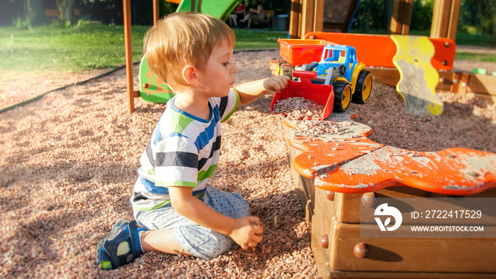 Portrait of little 3 years old toddler boy sitting on the playground and digging sand with toy plastic spade