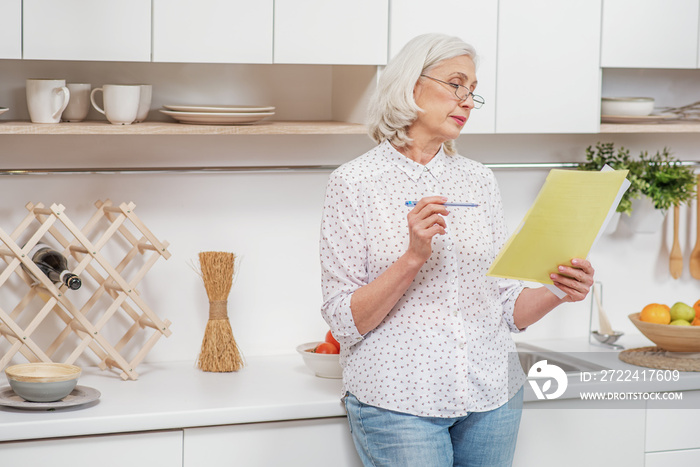 Serious mature woman reading document at home