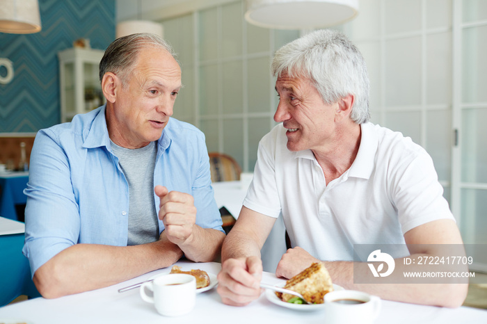 Communication of two friendly senior men by cup of tea and dessert in cafe