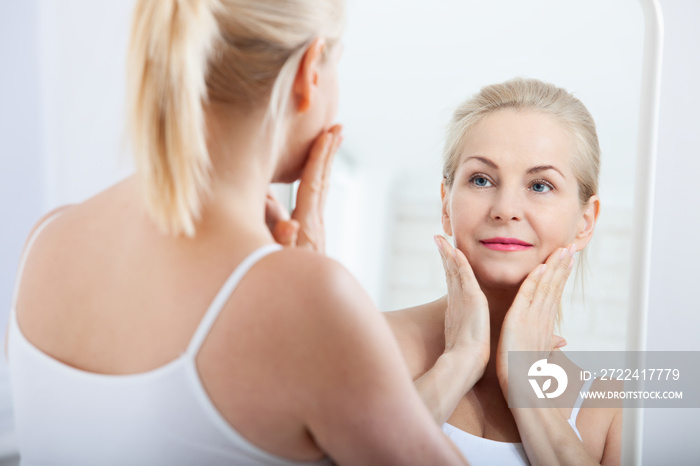 Middle aged woman looking at wrinkles in mirror. Plastic surgery and collagen injections. Makeup. Macro face. Selective focus