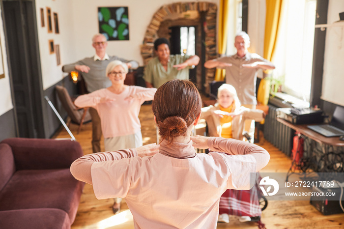 Back view at young woman coordinating group of senior people during morning exercises, copy space