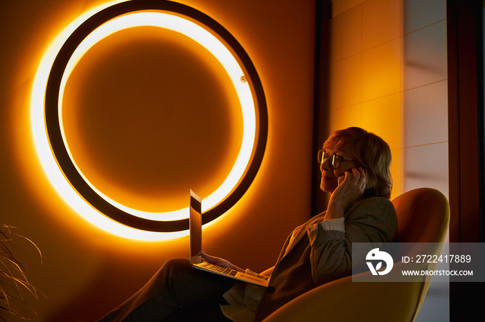 Senior citizen talking on phone near orange neon sign