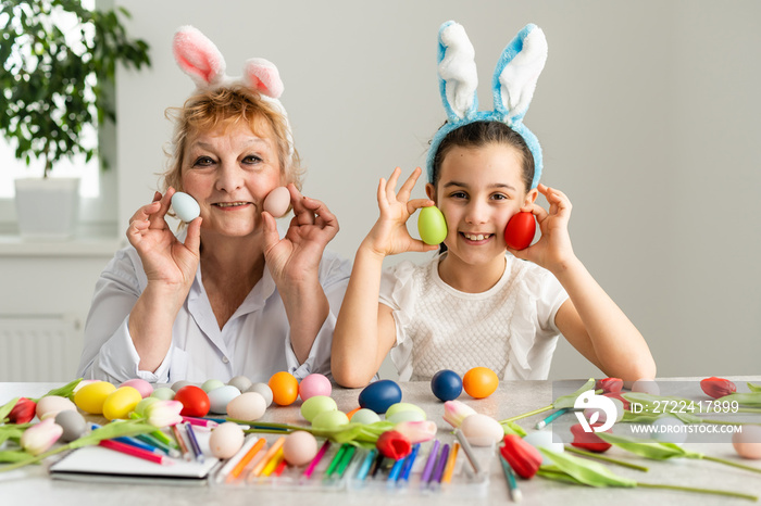 Easter concept. Grandmother with granddaughter are holding Easter eggs at home