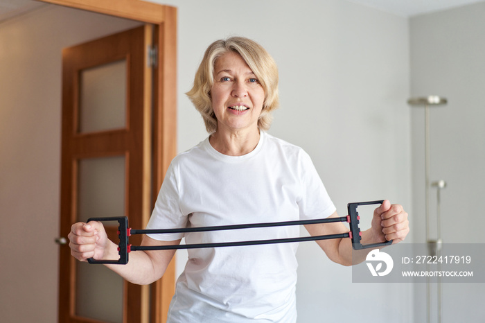 Home training concept. Strong senior woman doing exercises with dumbbells indoors. Cheerful mature lady working out her arm muscles, keeping fit, leading healthy lifestyle