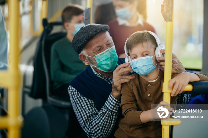 Happy boy enjoying in music over headphones while commuting by bus with is grandfather.