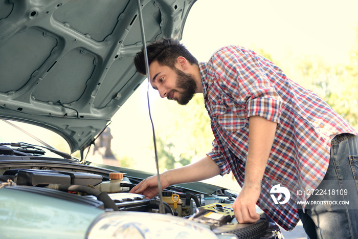 Young handsome man looking under car hood