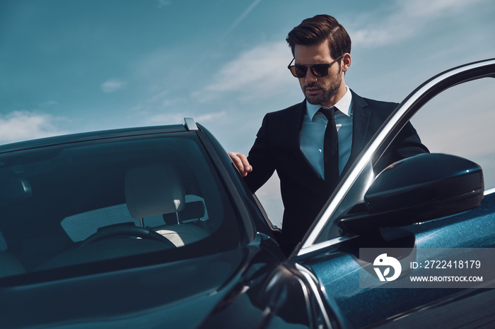 Time is money. Handsome young man entering his car while standing outdoors