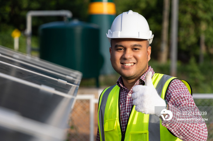 Young asian electrical engineer standing in front of Solar cell panels farm. He showing thumbs up. Solar generator power concept.