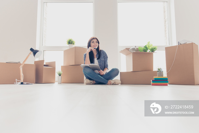 Low angle photo of brunette young woman in light modern apartment, looking up and dreaming, planning how she will organize the space in new apartment