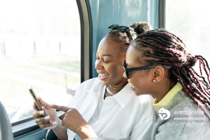 Young female friends riding city bus and using phone