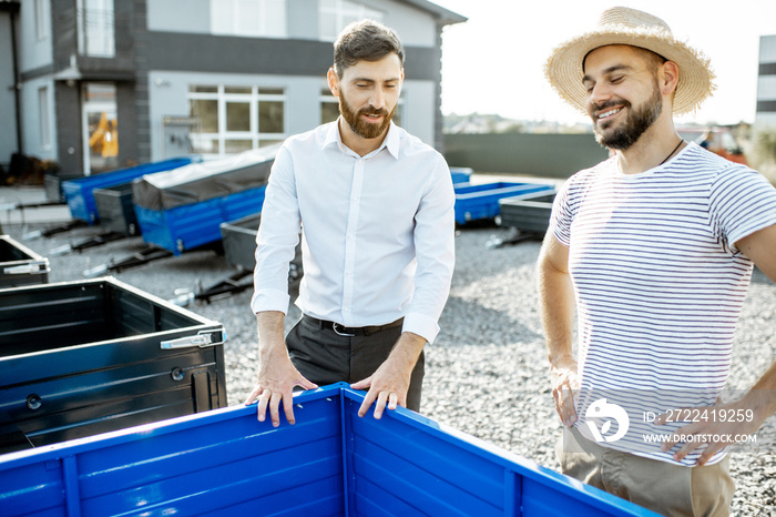 Agronomist with salesman choosing a new farm truck trailer, standing on the open ground of the agricultural shop