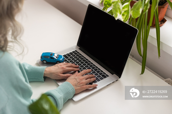 Sales woman is recording document on a laptop with car models and notebooks on the desk, concept of selling contracts.