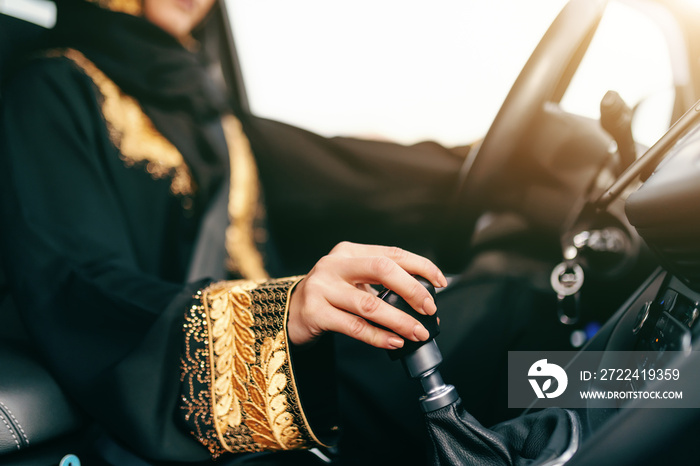 Close up of muslim woman holding hand on gearshift while driving car. Selective focus on hand.