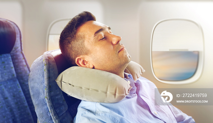 travel, comfort and people concept - man sleeping in plane with inflatable cervical neck pillow over porthole background