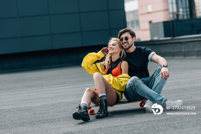 Woman and handsome man in glasses sitting on skateboard