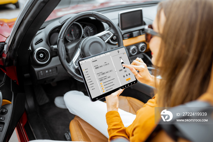 Young woman controlling car using a digital tablet and mobile application while sitting on the driver’s seat, view from the backside