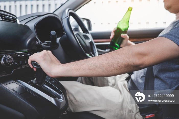 Young asian man drives a car with drunk a bottle of beer behind the wheel of a car