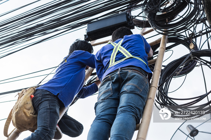 Electrical linemam worker climb a bamboo ladder to repair wire. A telecom engineer installing wire for internet.