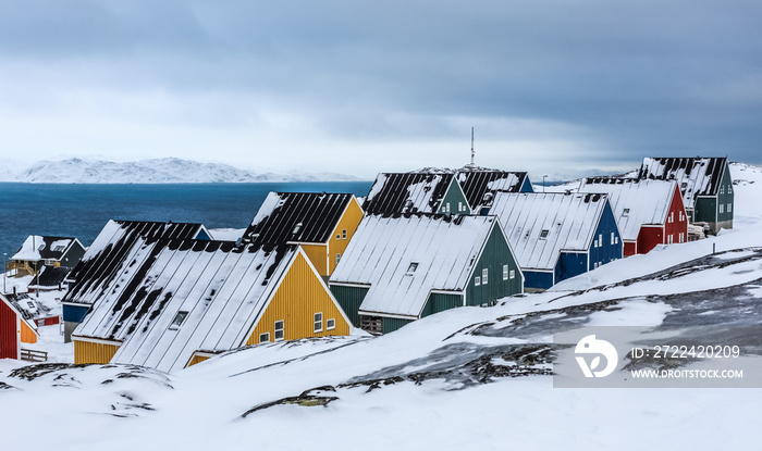 Yellow, blue, red and green inuit houses covered in snow at the fjord of Nuuk city, Greenland