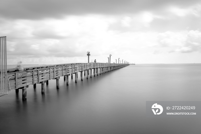 Long exposure wooden fishing pier stretching out over Galveston Bay in La Porte, Texas, USA. Foot pier for saltwater fishing with motion blurred people, recreation concept. Nature seascape background