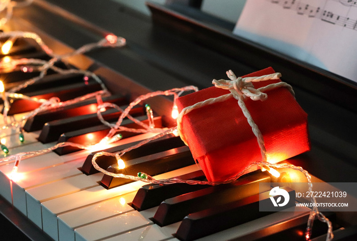 Red gift box with string lights glowing on piano keyboard.