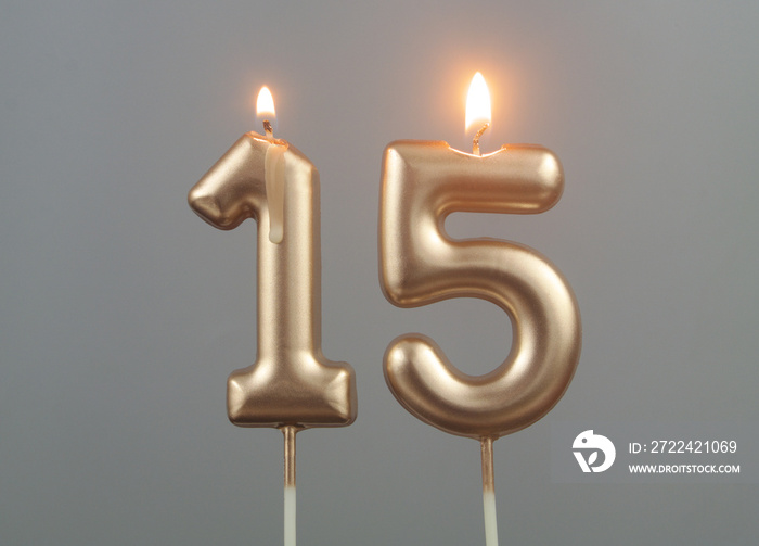 Burning gold birthday candles on gray background, number 15