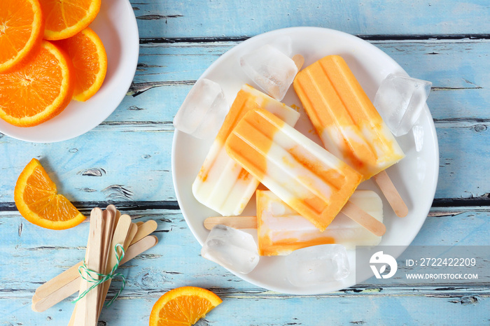 Healthy orange yogurt popsicles on a plate, top view table scene against a blue wood background