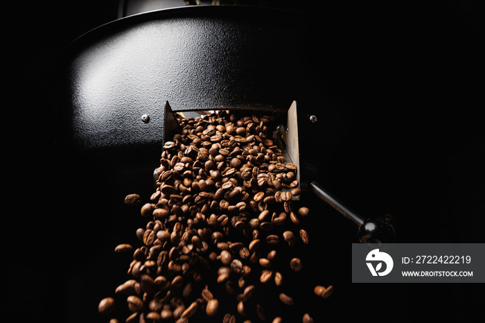 Fresh roasted coffee beans move on professional mixing roaster machines, dark background