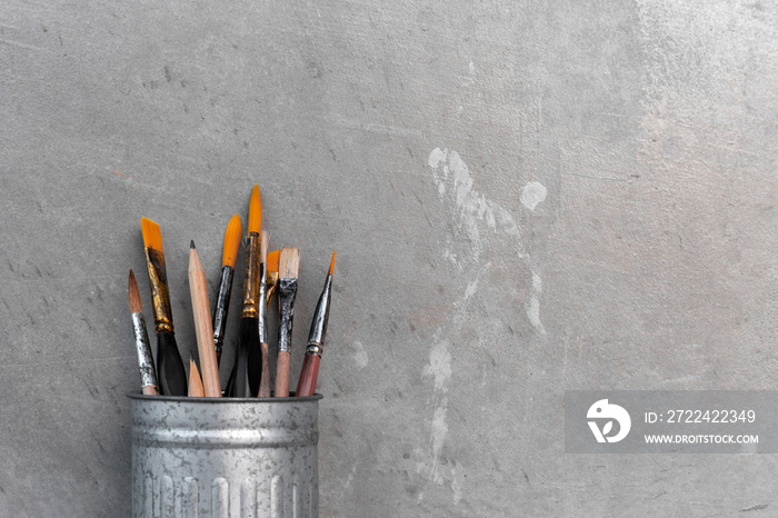 closeup of paint brushes in dirty old metal jar with cement background