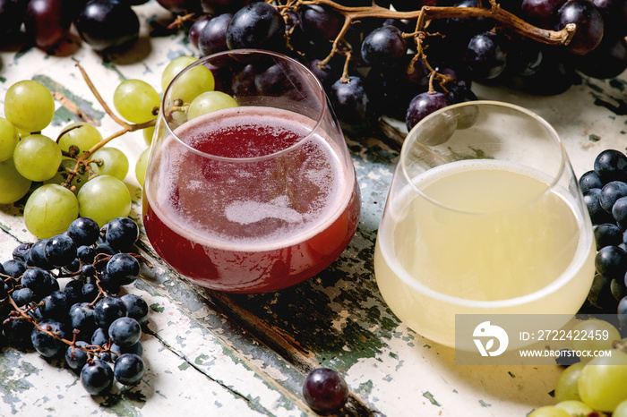 Traditional New european low alcohol red and white wine Federweisser or Neuer Wein, Burcak, Vin bourru in glasses with black and green grapes bunches on old white wooden table.