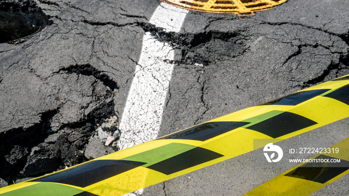 Dangerous stretch of road with damaged asphalt. The accident site is fenced off with black and yellow tape. The concept of repair or accident of sewerage, underground communications, water supply.